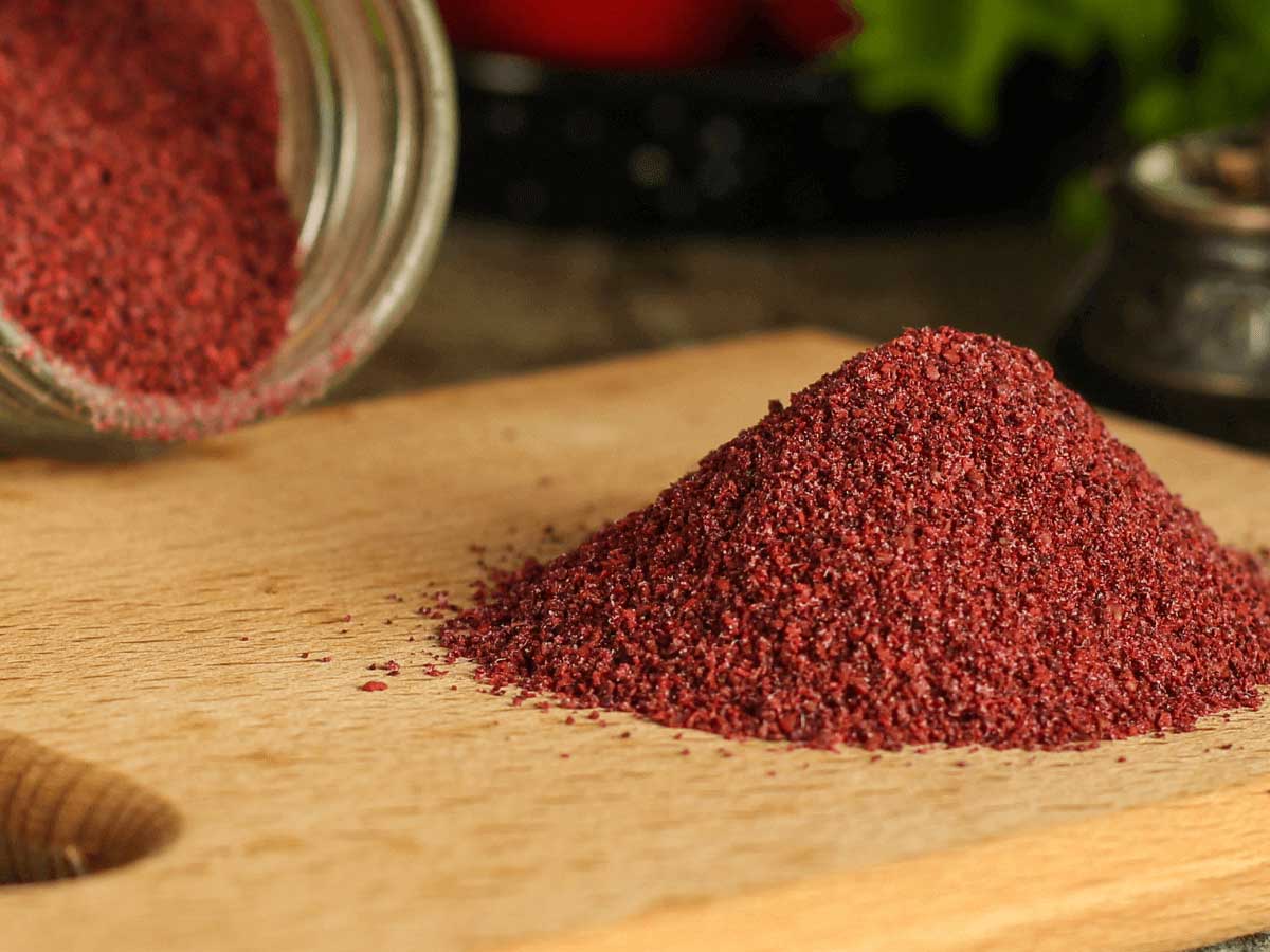 Image shows sumac spice on a wooden cooking board.